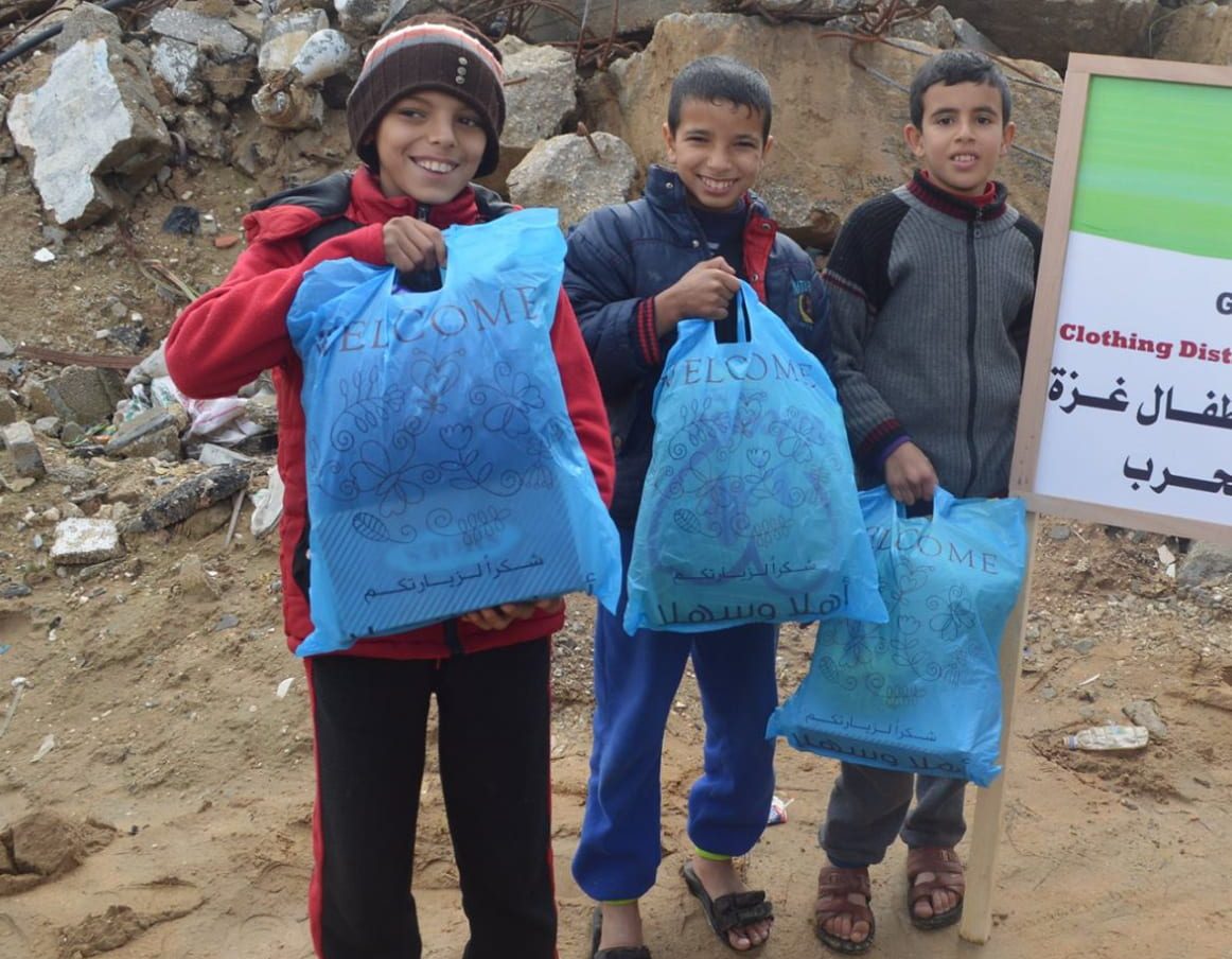 Three children in Gaza holding bags of new clothes